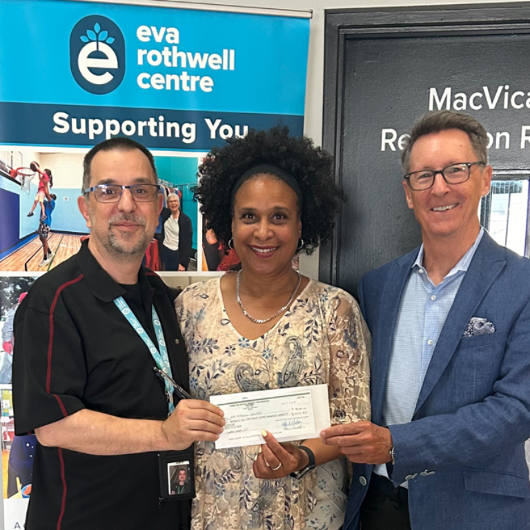 Three people holding a check in front of an Eva Rothwell Center sign