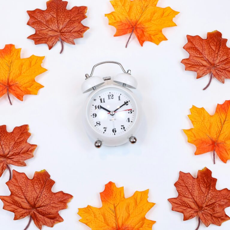 Brown and orange maple leaves around an old-timey white clock on a light background